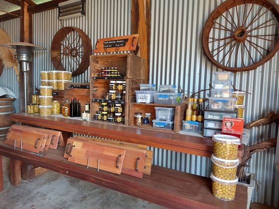 A timber bench inside the shed set up as a shop stall with jars of olives, oils and local produce for sale.